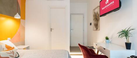 A modern hotel room with a bed, a desk, a chair, and a TV displaying the barrooms sign.