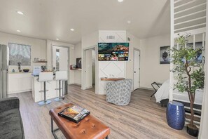A modern living room with a television mounted on the wall displaying a movie selection. There is a seating area with a bench and a small table, and a potted plant on the right. - Medicine Park Flat's #08 (Medicine Park)