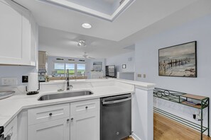 Uma cozinha moderna com ilha central, máquina de lavar louça embutida e uma grande janela com vista panorâmica.