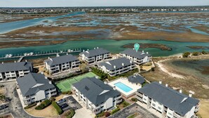 Una vista aerea di una zona residenziale costiera con diversi condomini, un porto turistico con imbarcazioni e una vasta distesa d'acqua.