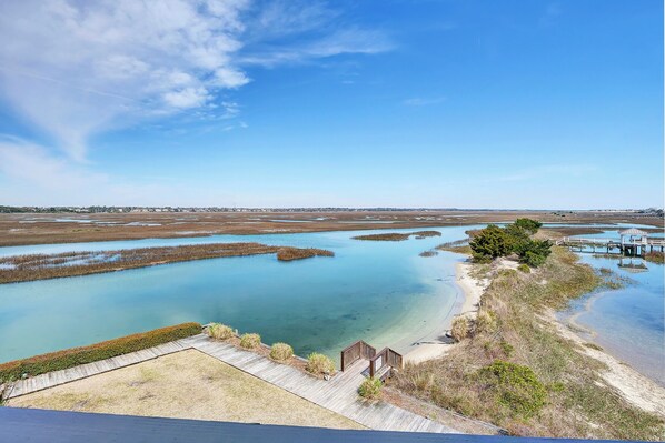 A coastal landscape with clear water, a wooden walkway, and a small structure near the water's edge.