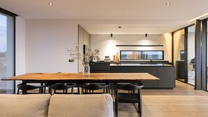 Eine moderne Küche mit einer zentralen Kochinsel, einem Essbereich mit Holztisch und -stühlen sowie einer Couch im Vordergrund.