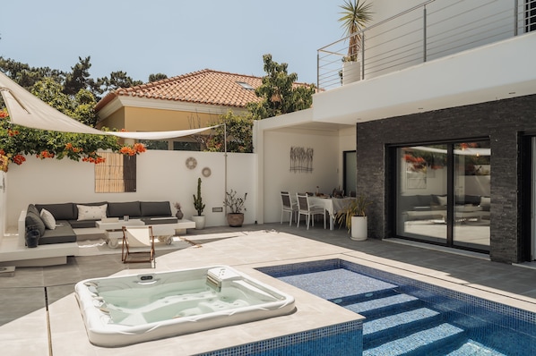 Un espace de vie extérieur moderne comprenant un jacuzzi, une piscine et un coin repas avec une table et des chaises.