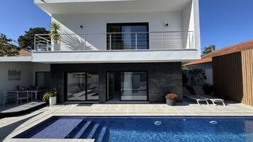 A modern two-story house with a swimming pool, a balcony, and a patio area.