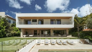 A modern two-story house with a swimming pool, outdoor seating, and lush greenery.