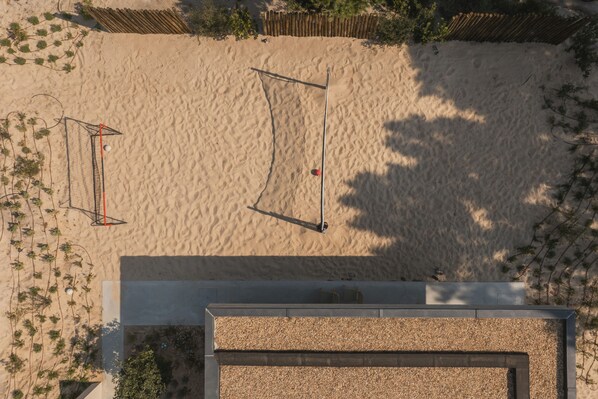 Luchtbeeld van een zandstrand met volleybalnetten en een gebouw met een stenen gevel.