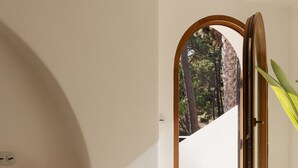 Un dormitorio minimalista con una cama, una lámpara de noche y vistas a un bosque a través de un ventanal abierto.
