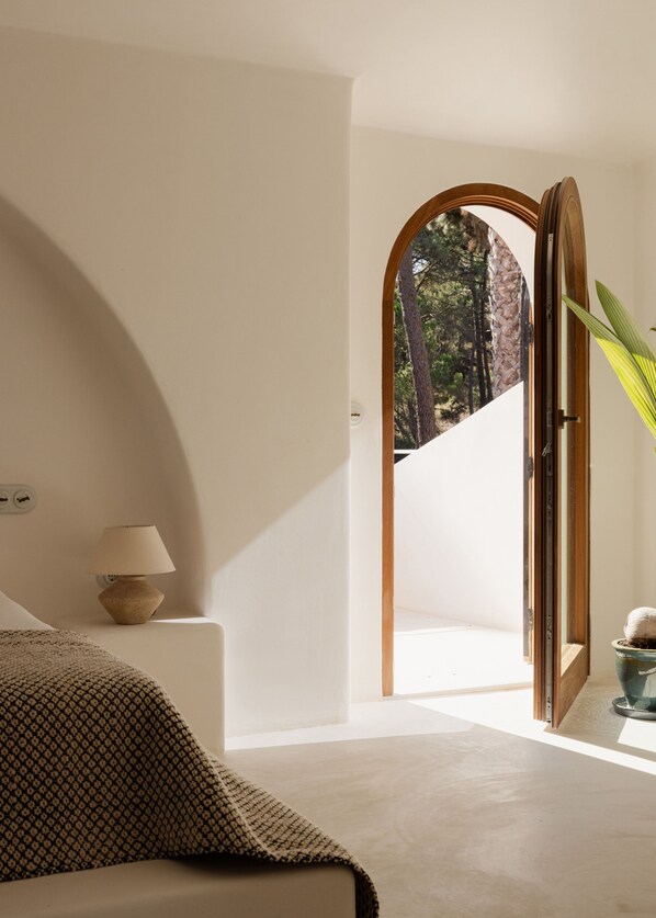 A minimalist bedroom with a bed, a bedside lamp, and a view of a forest through an open door. - Elysian Villa by Cadenzalux (Almada)