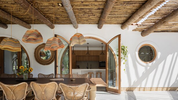 Un comedor con sillas de mimbre y una mesa de madera, una cocina con armarios de madera y un ventanal redondo.