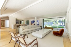 A spacious living area with a large sofa, a coffee table, and a unique orange chair. - Havenwood Villa by Cadenzalux (Cascais)