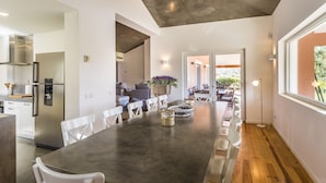 A modern kitchen with a long dining table, white chairs, and a view to the outdoor patio. - Grandola Mountain Paradise by Cadenzalux (Grandola)