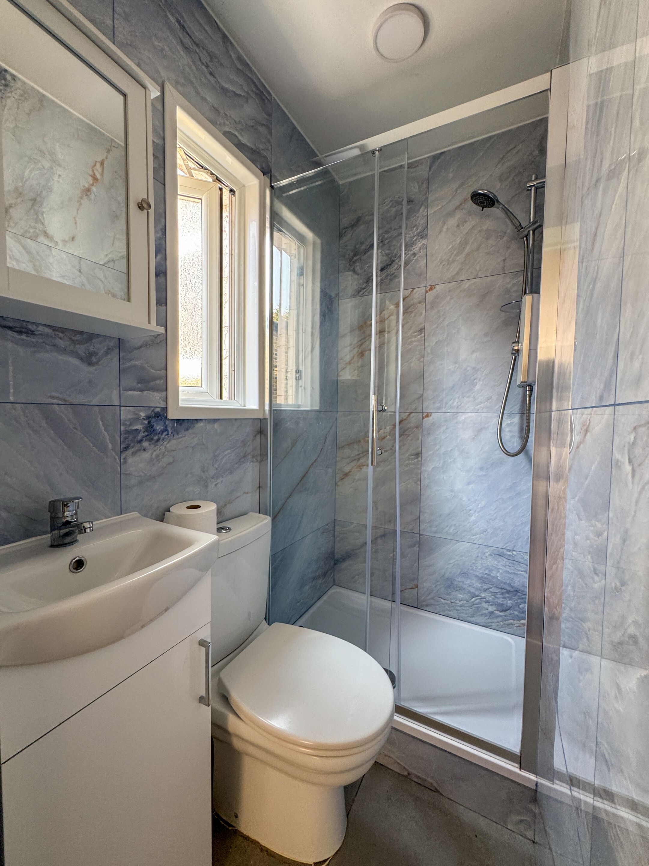 A bathroom with a marble wall, a toilet, a sink, and a glass-enclosed shower.