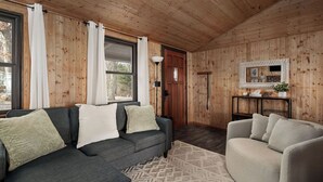 Un accogliente soggiorno con un divano grigio scuro, una poltrona beige e un tappeto decorato. Si notano inoltre pannelli in legno e una porta con uno specchio sopra.