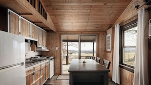 Interno di una baita in legno con angolo cottura, sala da pranzo e ampie finestre.