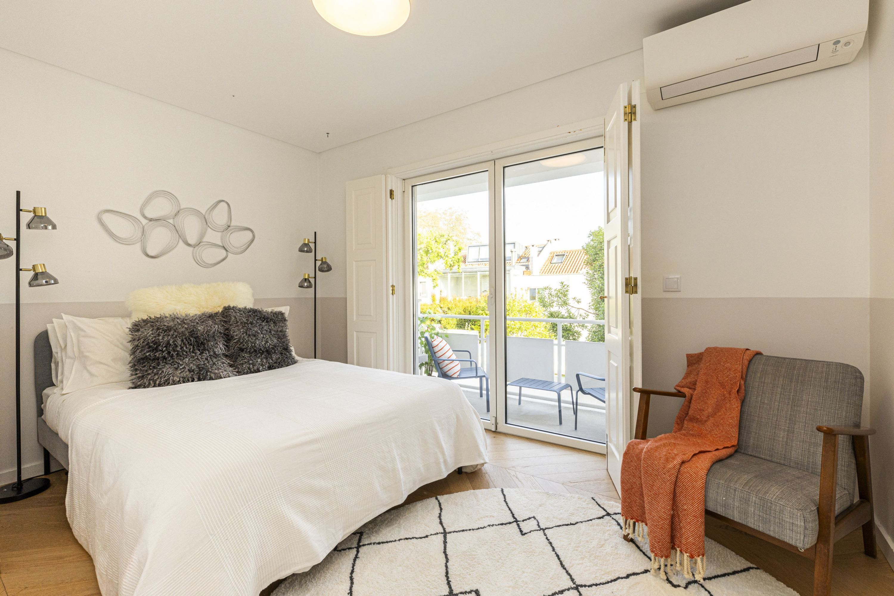 Un dormitorio con cama, una silla, un ventanal grande y un aire acondicionado instalado en la pared.