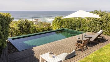 Relax by the ocean with a pool surrounded by lush greenery and comfortable lounge seating.
