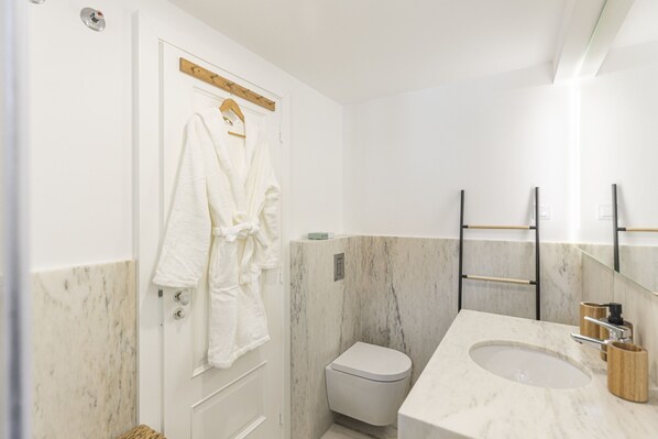 Un baño con lavamanos de mármol, un inodoro y una bata colgada en la puerta.