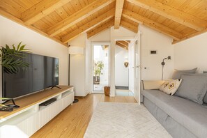A modern living room with a wooden ceiling, a flat-screen TV on a wooden stand, a grey sofa with cushions, and a white rug.