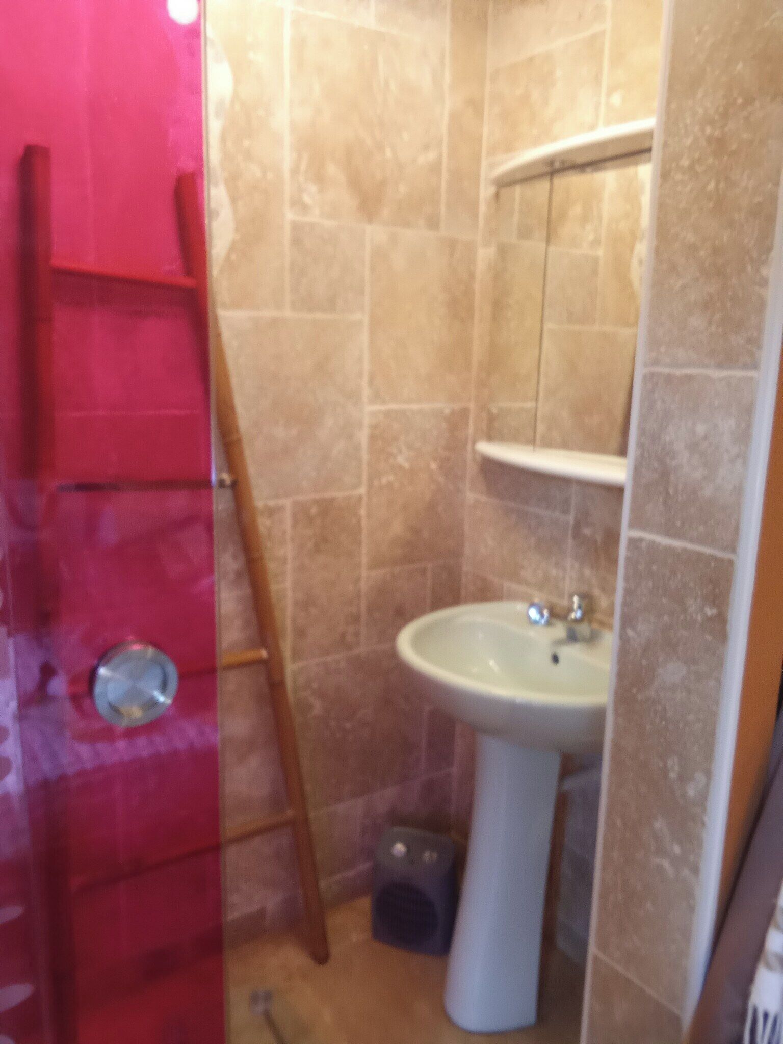 A bathroom with beige tiles, a white sink, and a red ladder leaning against the wall.