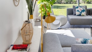 Een moderne woonkamer met een grijze bank, een salontafel met tijdschriften, een groot raam met uitzicht op de oceaan en een decoratieve spiegel aan de muur.