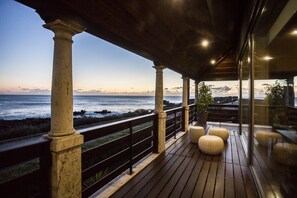 A wooden deck with columns and a railing overlooking the ocean at dusk.