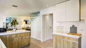 Una cocina moderna con armarios de madera, una isla central y una escalera que sube a un nivel superior.