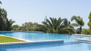 Una piscina azul cristalina con bordes de azulejos, rodeada de abundante follaje y palmeras.