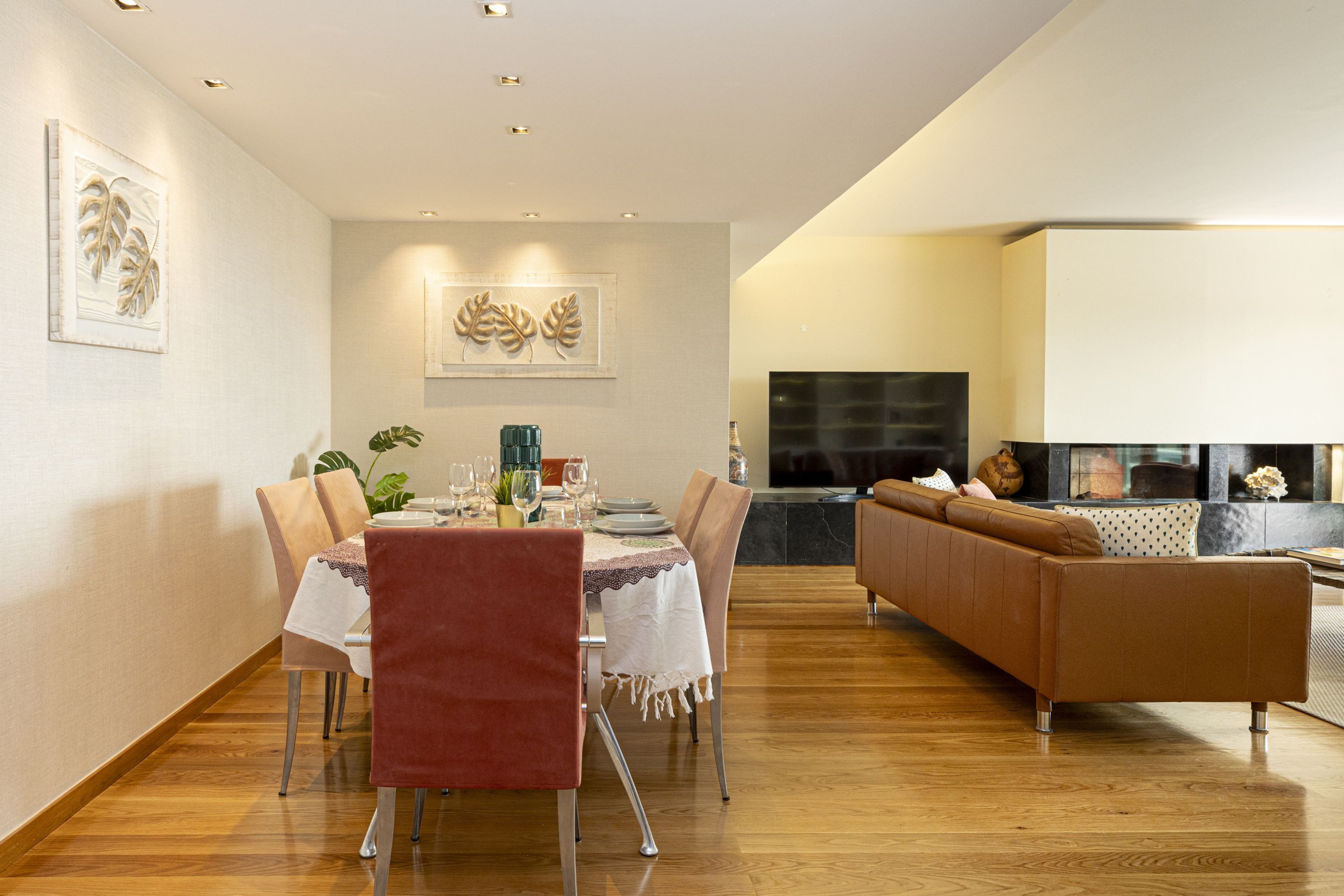 Un espace de repas moderne avec un plancher en bois, une table à manger entourée de chaises et un canapé en arrière-plan.