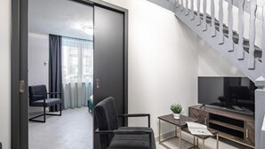 A modern living room with a sofa, a coffee table, and a TV. There is a staircase with a railing and a door leading to another room. - Dessewffy Premium Apartment (Budapest)