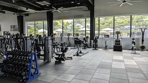 Un gimnasio con diverso equipo de ejercicio, ventanas amplias y una frase motivacional en la pared.