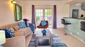 Una sala de estar con sofá, sillón, mesa de centro y una zona de bar con un asiento.