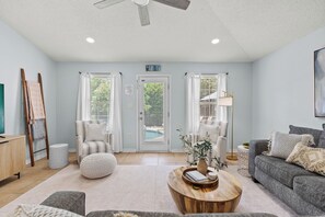 A spacious living room with a sofa, armchair, and coffee table. A door labeled "Beach House" leads to a pool area.
