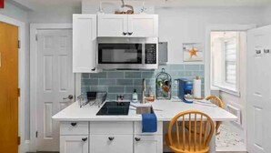 A compact kitchen with white cabinets, a microwave, and a small dining area with a wooden chair.