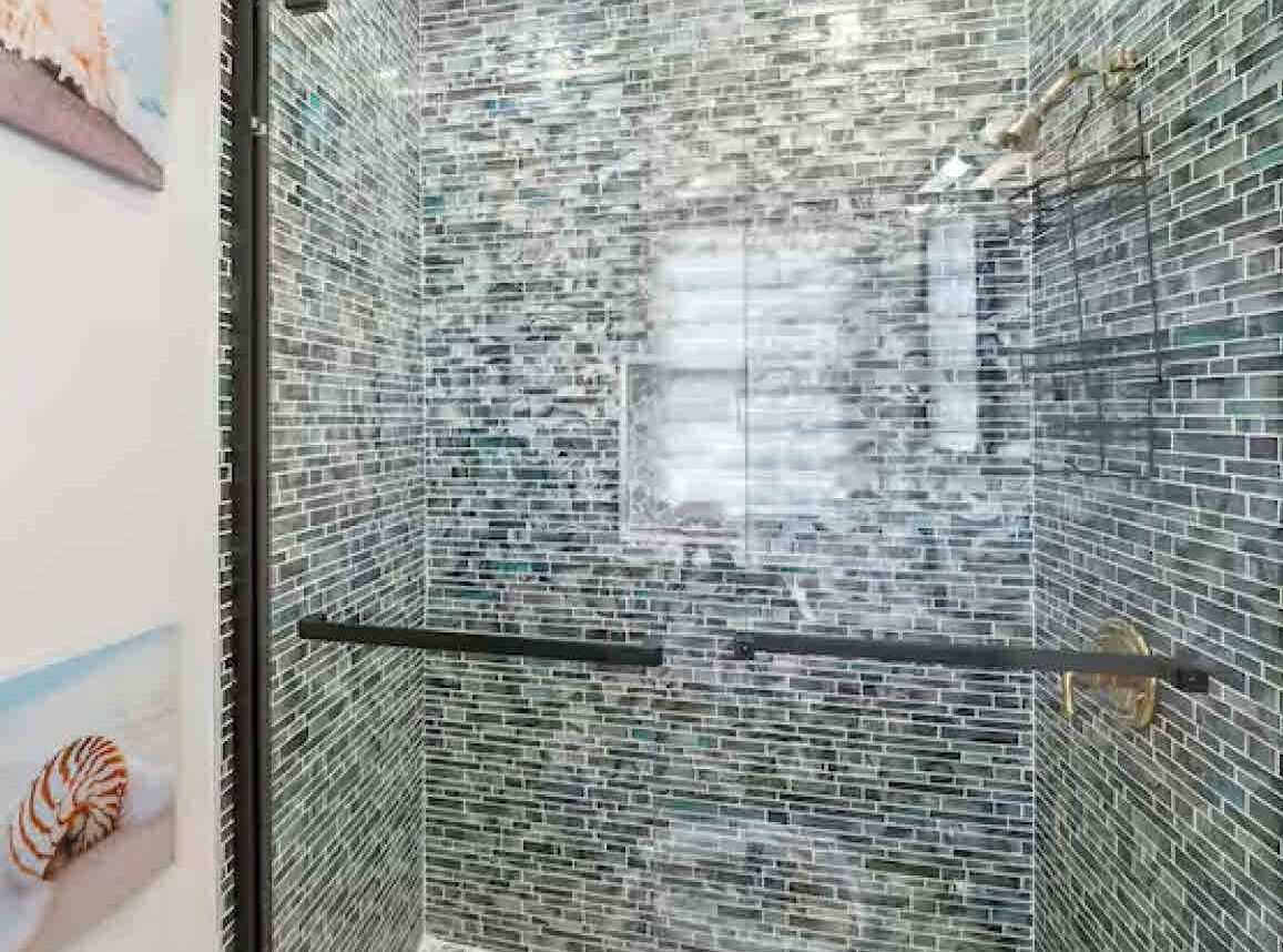 A bathroom with a tiled wall and a glass shower enclosure.