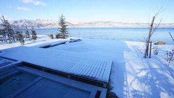 Un espace extérieur enneigé comprenant une piscine, une terrasse en bois et une vue sur un lac et des montagnes.