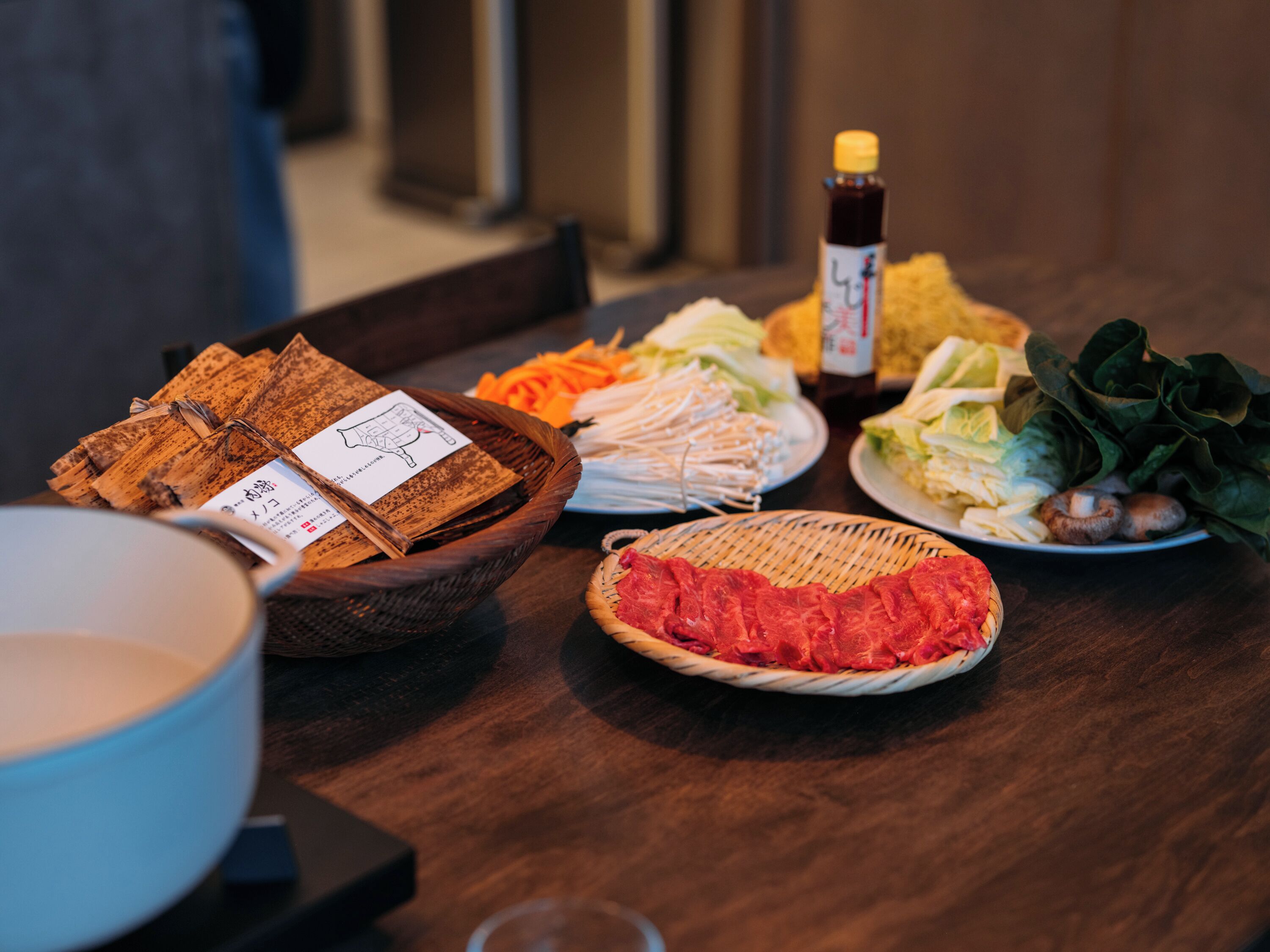 A table with various food items including a basket of bread, a plate of vegetables, and a dish of raw meat.