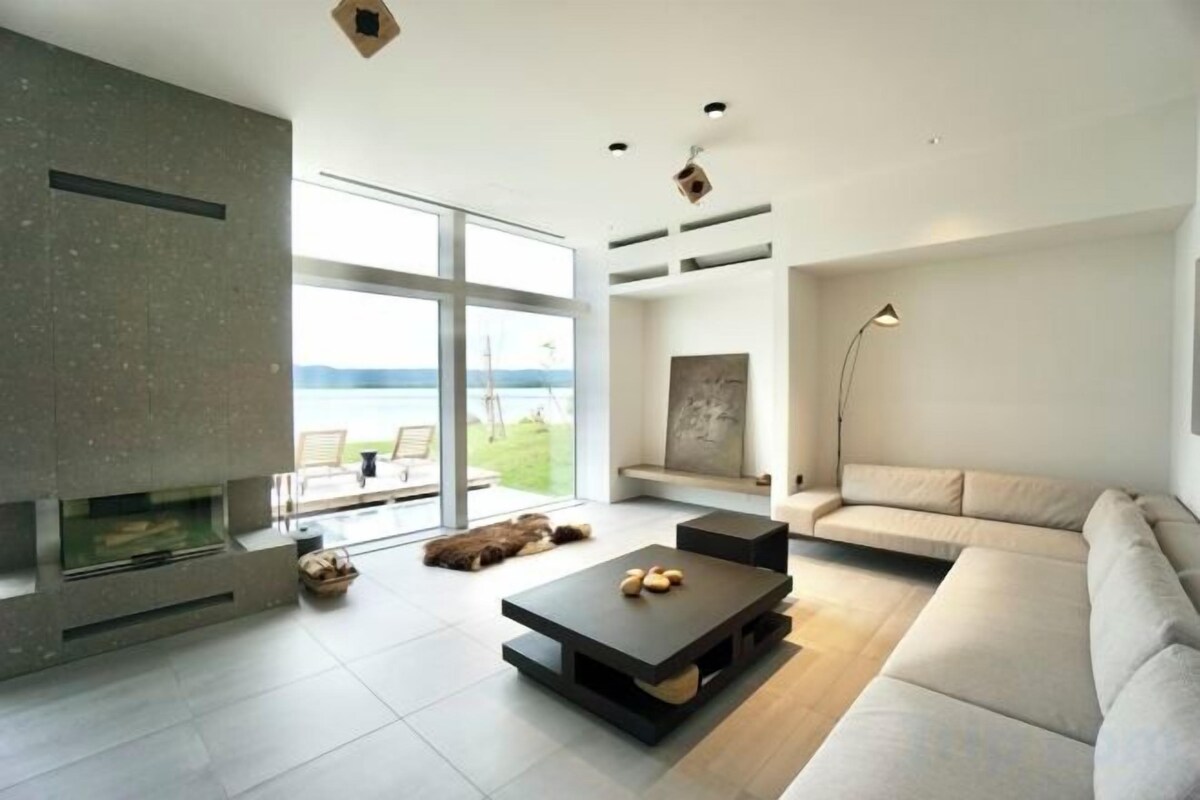 Ein modernes Wohnzimmer mit Kamin, einer Couch, einem Couchtisch und Blick ins Freie.