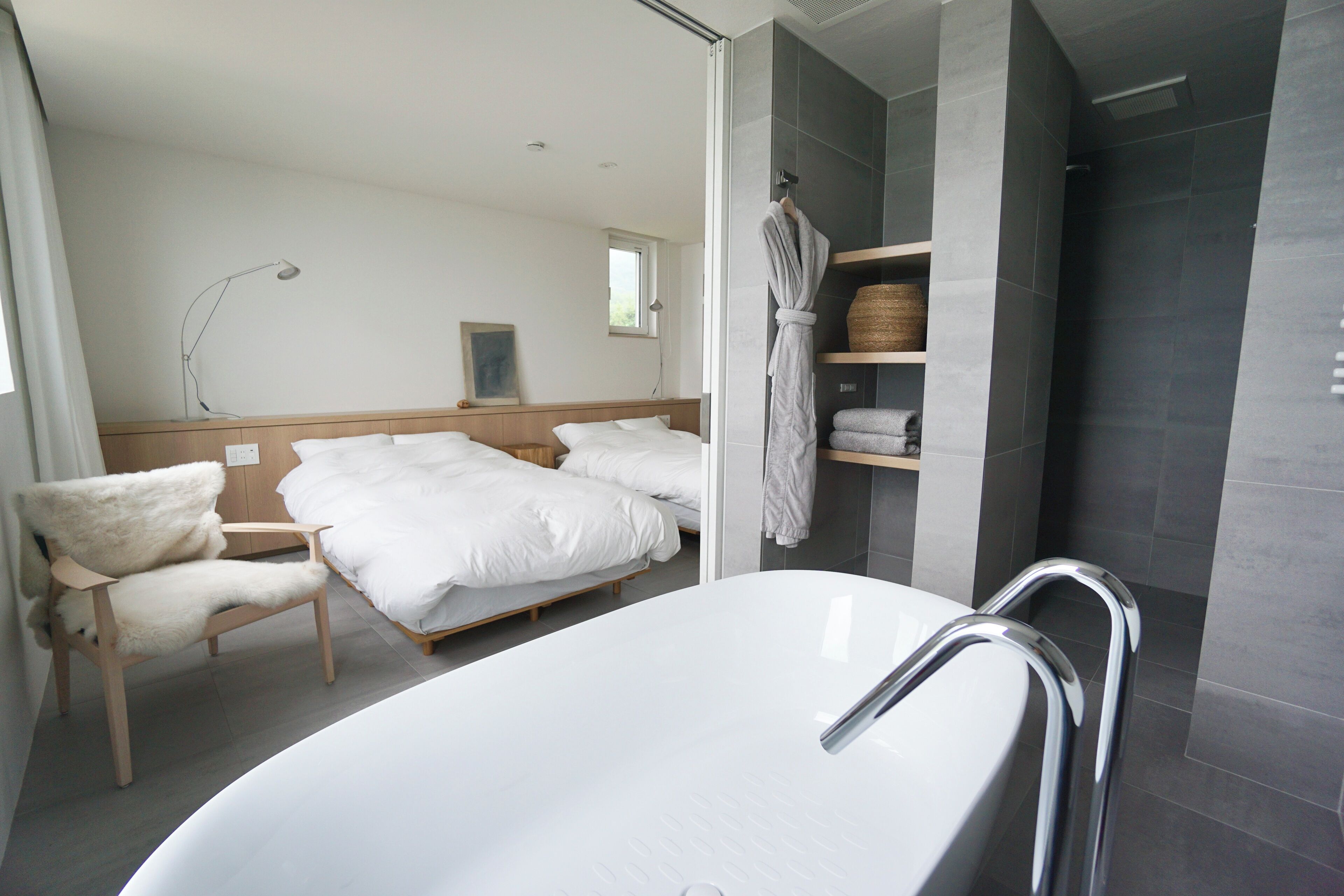 A modern bathroom with a bathtub, a shower area, and a bed with white linens.