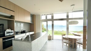 A modern kitchen with a central island, built-in oven, and a view of the outdoors through large windows. - Sansui Lakeside Villa (Teshikaga)