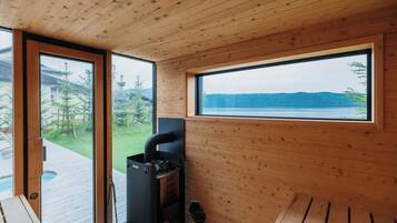 Una cabaña de madera con sauna, ventanas amplias y vista al lago.