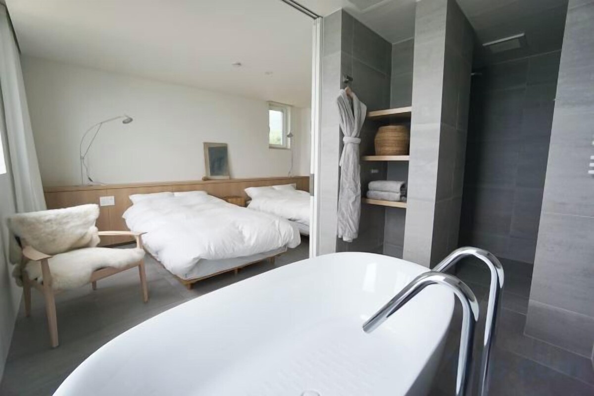 A modern bathroom with a freestanding bathtub, a wooden bed, and a robe hanging on a rack.