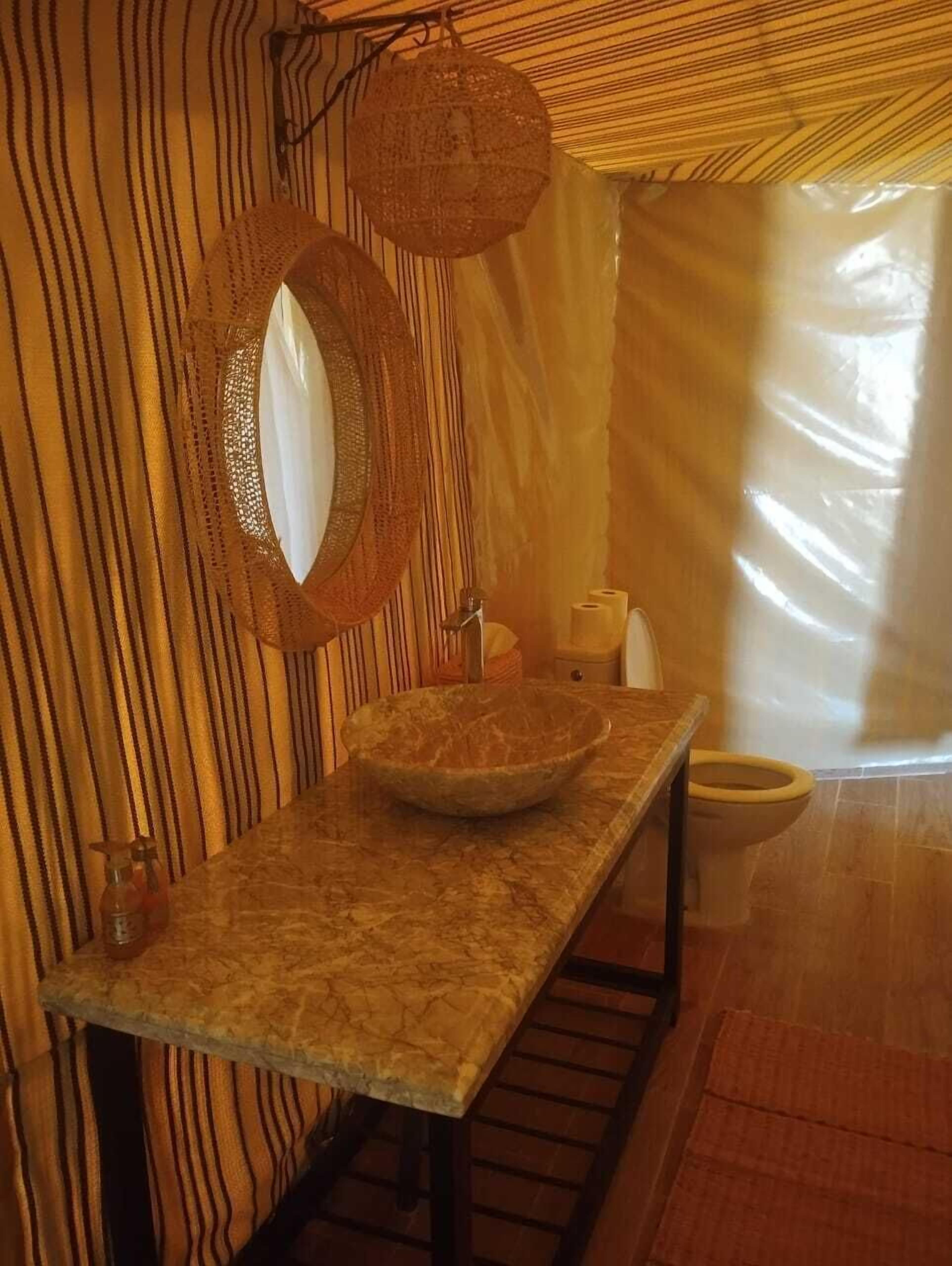 A bathroom with a wooden vanity, a round mirror, and a large bowl sink.