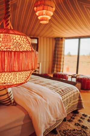 Une chambre avec un grand lit, une lampe suspendue et une vue sur le désert par la fenêtre.