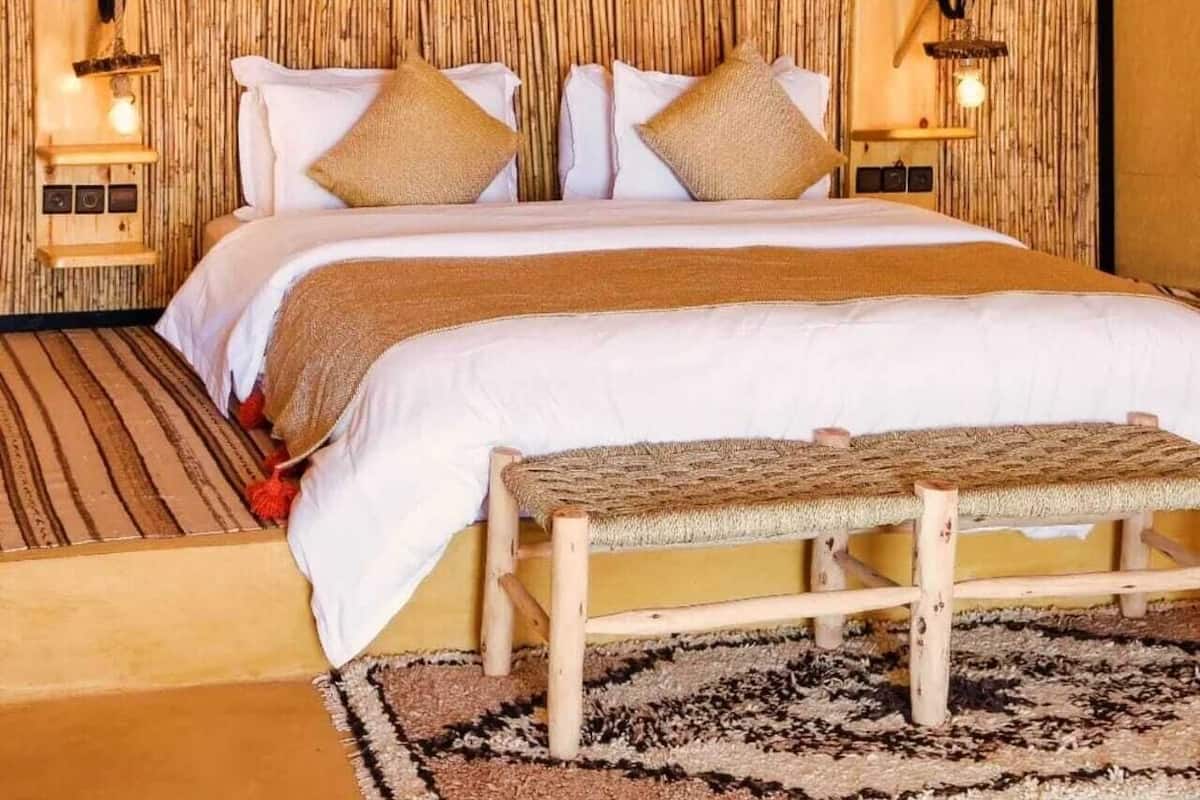 Een bed met hoofdeinde, kussens en nachtkastje met lamp.