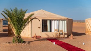 Een tent in de woestijn met een rood tapijt, twee stoelen en een palmboom.