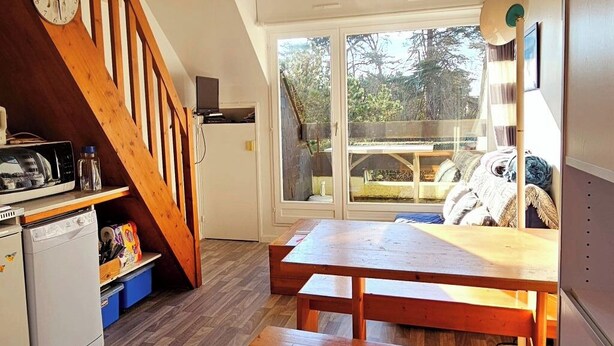A compact kitchen with a wooden staircase, a dining area with a table and benches, and a large sliding glass door leading to an outdoor deck. - Bright apartment between port and beaches (Arzon)