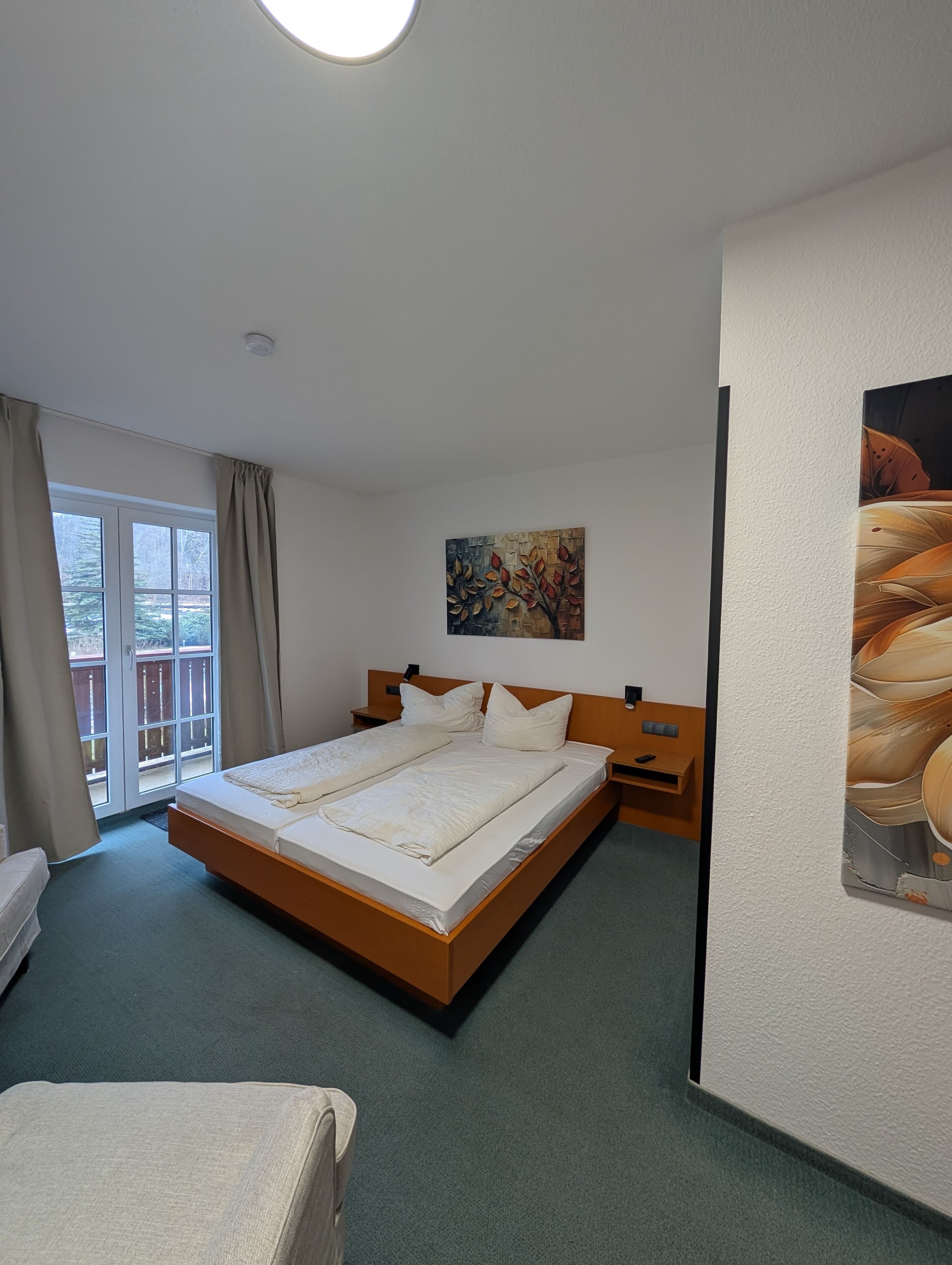 Ein Hotelzimmer mit einem großen Bett, einem Bild an der Wand und Blick ins Freie durch das Fenster.