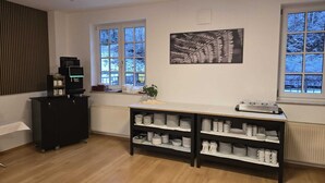 Une cuisine moderne avec un plancher en bois, un meuble noir contenant des appareils électroménagers et un comptoir blanc doté d’étagères où sont rangés de la vaisselle et un appareil à café.