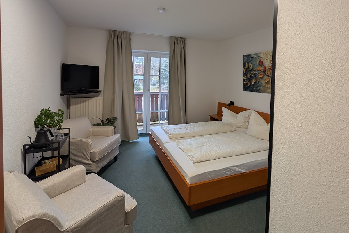 A hotel room with a bed, a sofa, a TV, and a window with curtains.