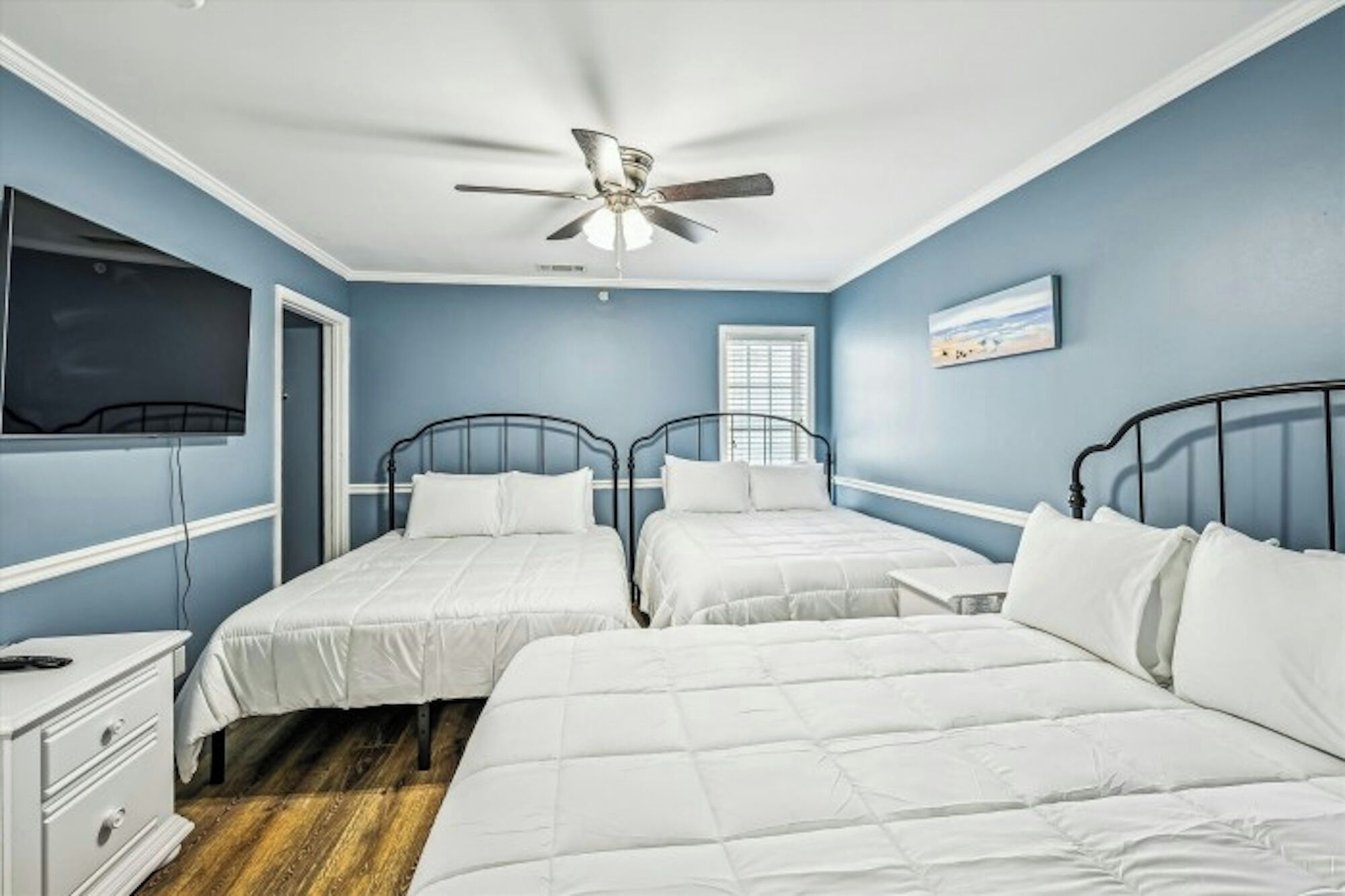 A bedroom with two beds, a ceiling fan, a TV, and a window with blinds.